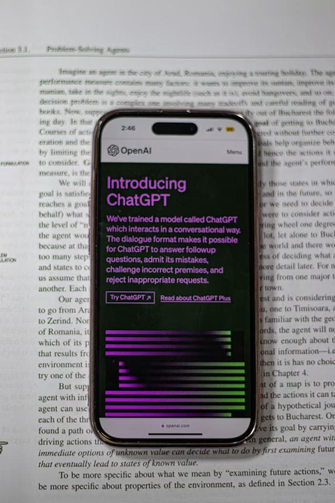 Mobiltelefon med teksten Introducing ChatGPT holdt over en trykt avisside