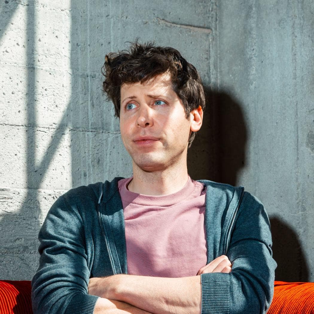 Sam Altman sitter med armene i kors i rosa T-skjorte på en rød sofa